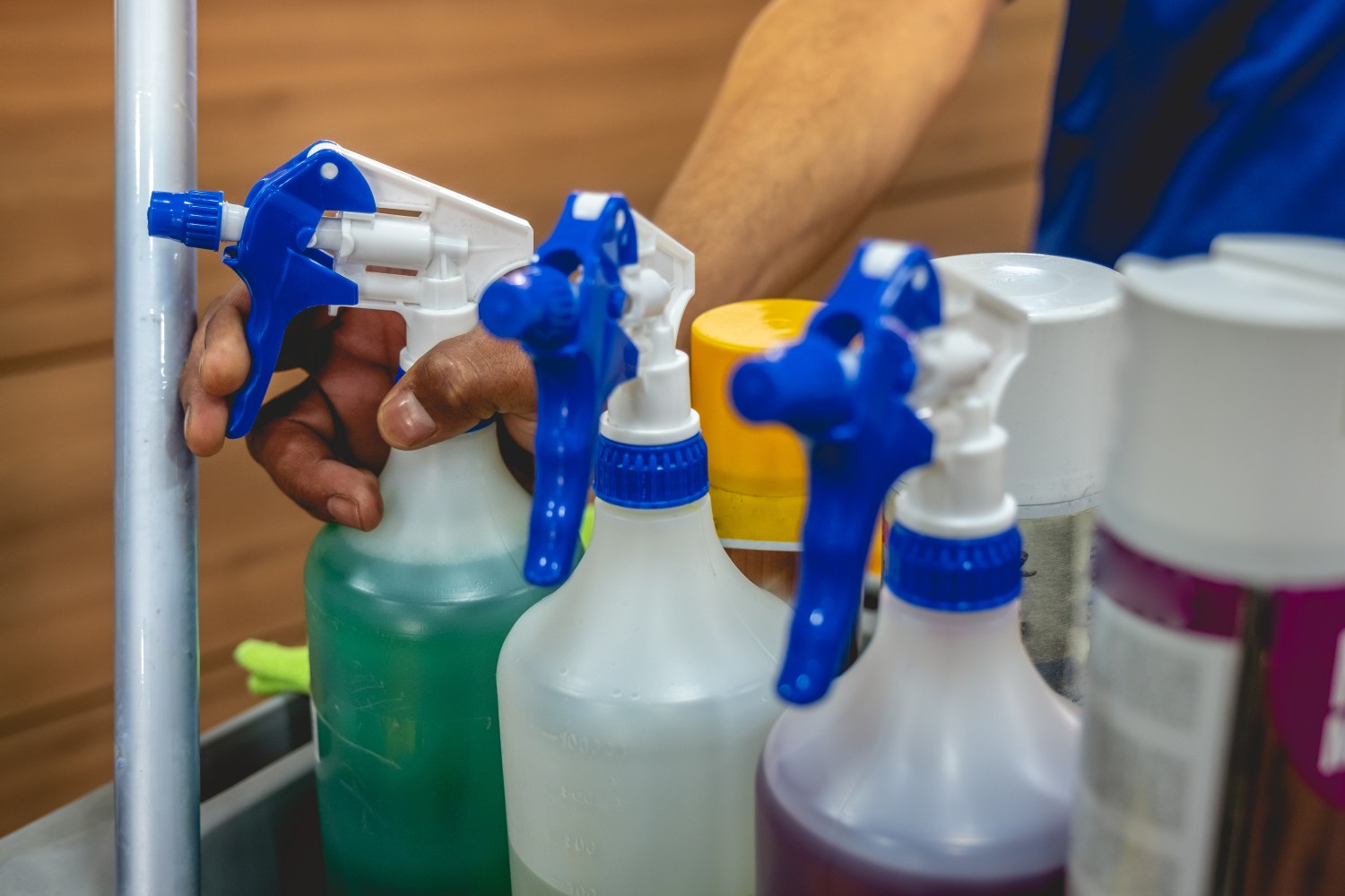 Hand of young janitorial services worker holding a sprayer with cleaner in trolley of cleaning supplies